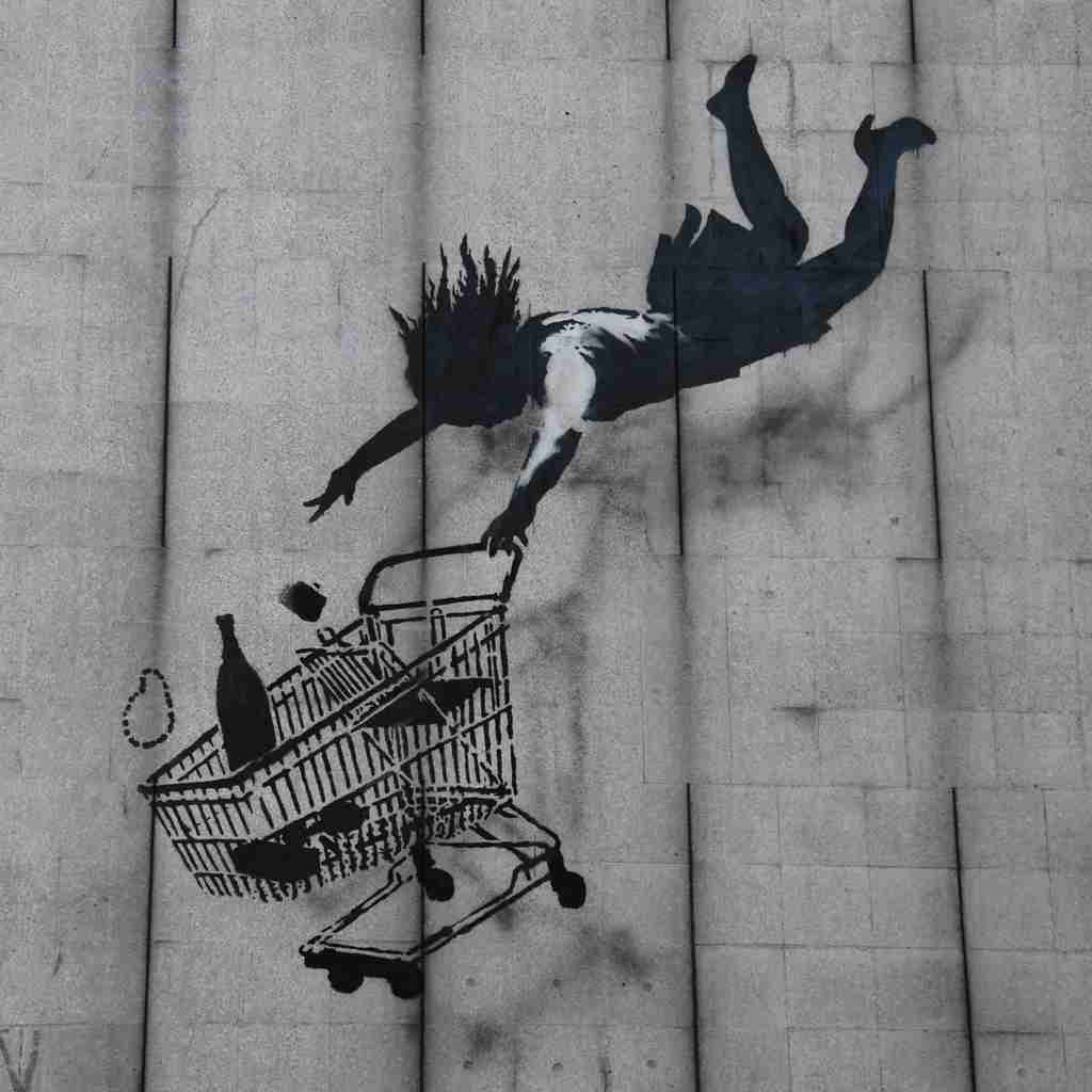 Shop till you drop, Banksy. Image of a woman falling into the void behind a shopping cart.
