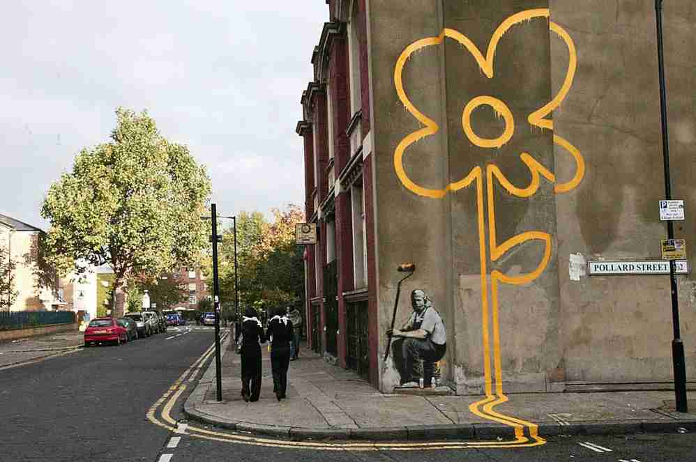 Yellow lines flower painter. Banksy's work on a London street depicting a painter in overalls and his roller, resting after having painted double lines on the pavement up the pavement and façade, culminating in a beautiful large flower.